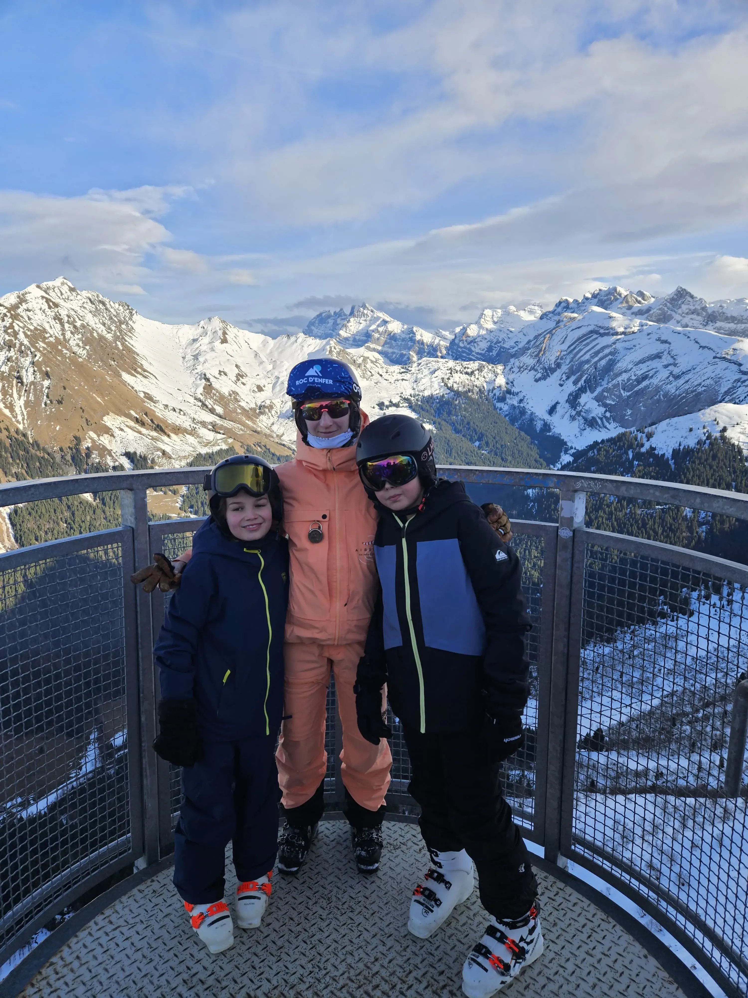 Sofia entre deux jeunes skieurs sur une plateforme panoramique, face aux sommets enneigés.